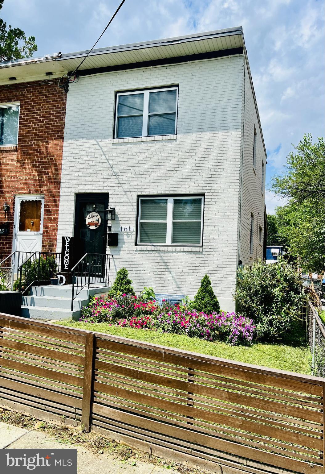 a front view of a house with lots of flowers and trees