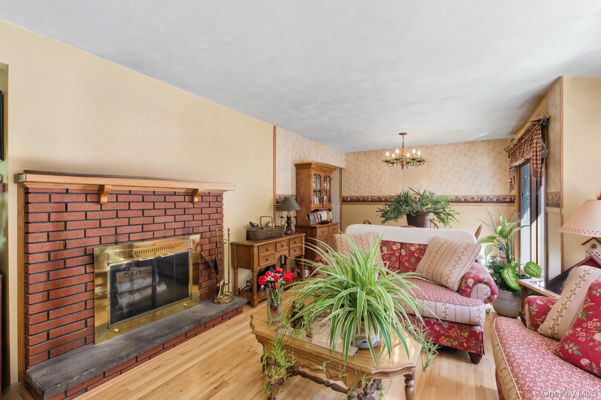 347 Wading River Road Manorville, NY 11949 - Photo 4 of 30 Living room with wood finished floors, a brick fireplace, wallpapered walls, and a chandelier