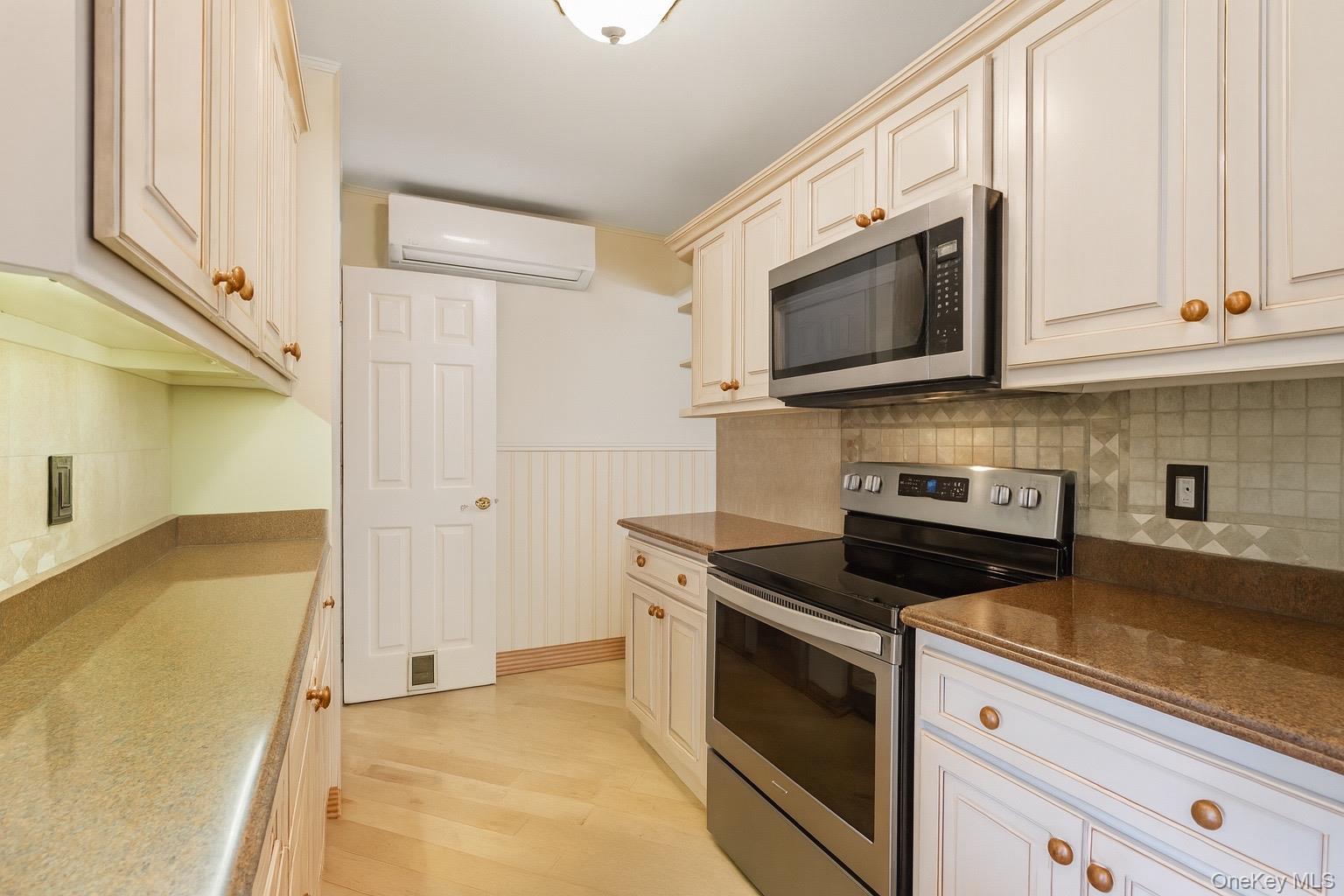 347 Wading River Road Manorville, NY 11949 - Photo 7 of 30 Kitchen featuring appliances with stainless steel finishes, wainscoting, light wood-style flooring, a wall mounted AC, and tasteful backsplash