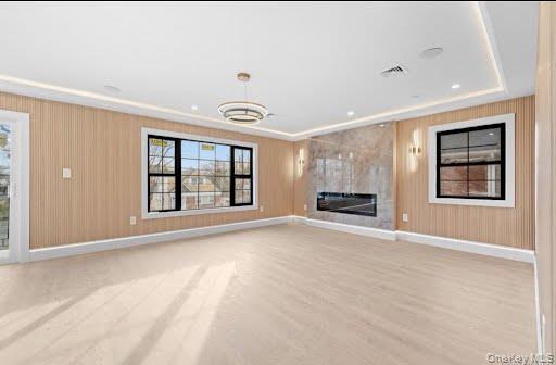 Spacious LIVING room featuring light wood-finish flooring, accent walls with vertical paneling, and an electric fireplace set within a large slab stone surround
