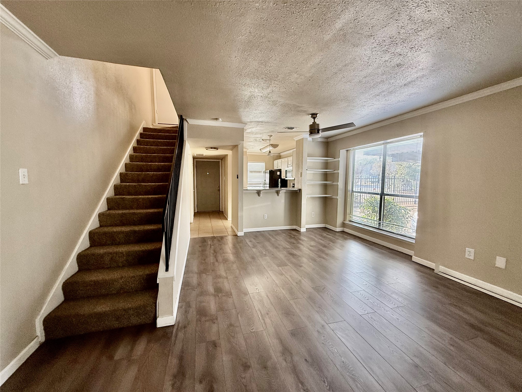 2018 West Rundberg Lane, Unit 6A Austin, TX 78758 - Photo 11 of 17 Unfurnished living room with a textured ceiling, dark wood finished floors, ornamental molding, and a ceiling fan