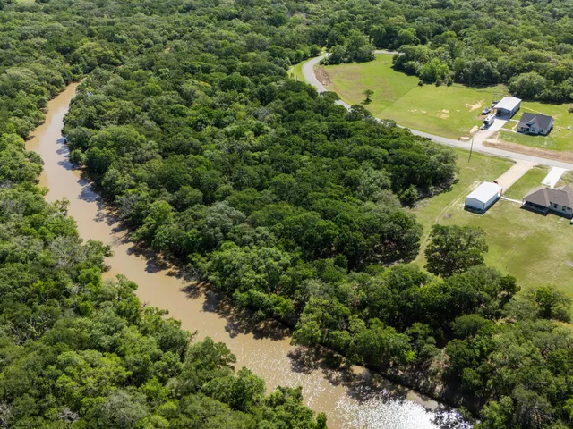 an aerial view of a residential houses with outdoor space and trees all around