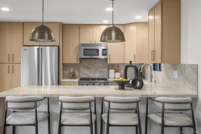 a kitchen with stainless steel appliances granite countertop a sink a stove a refrigerator and chairs