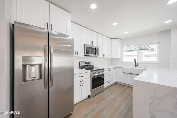 a kitchen with stainless steel appliances a sink a stove a refrigerator cabinets and a wooden floor