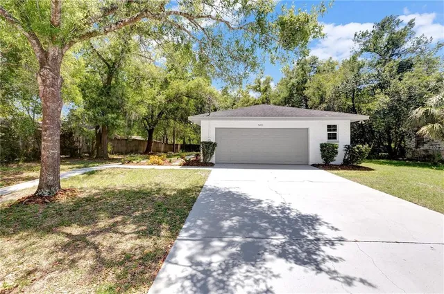 a view of a white house with a yard and large trees