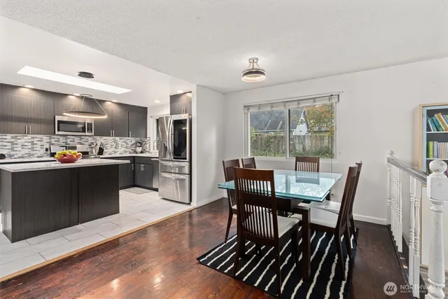 a kitchen with stainless steel appliances kitchen island granite countertop a dining table chairs and a refrigerator