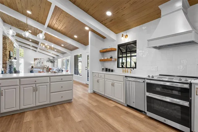 a large kitchen with stainless steel appliances granite countertop a large stove a sink dishwasher and white cabinets with wooden floor