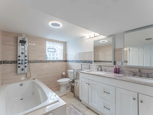 a bathroom with a double vanity sink a toilet a mirror and bathtub