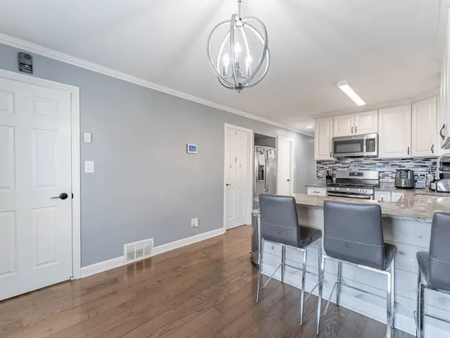 a kitchen with stainless steel appliances granite countertop a microwave a stove a sink dishwasher and white cabinets with wooden floor