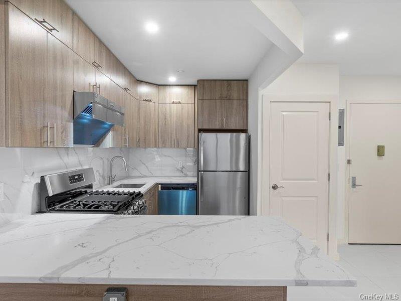 124-28 Queens Boulevard, Unit 6C Queens, NY 11415 - Photo 5 of 7 Kitchen with light stone counters, stainless steel appliances, backsplash, exhaust hood, and a peninsula