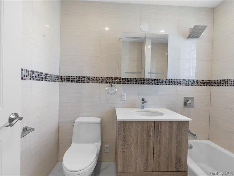 124-28 Queens Boulevard, Unit 6C Queens, NY 11415 - Photo 6 of 7 Full bath featuring tile walls, vanity, and bathtub / shower combination