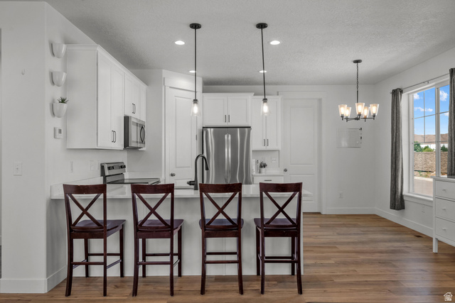 1693 North Center Point Lane Salem, UT 84653 - Photo 4 of 26 Kitchen featuring a breakfast bar with pendant lighting, white cabinetry, stainless steel appliances, and wood-finish flooring