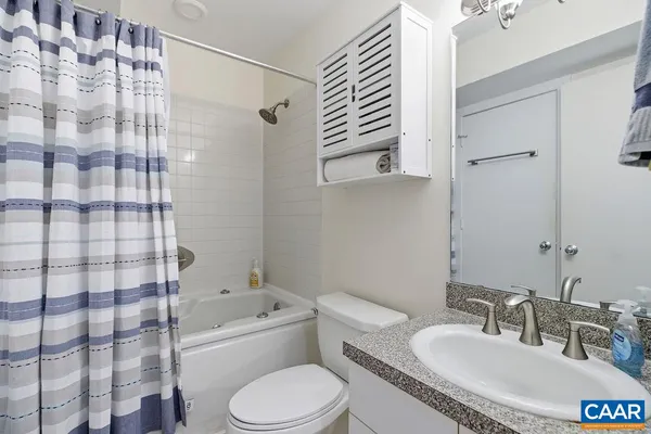 a bathroom with a granite countertop bathtub sink vanity mirror and toilet