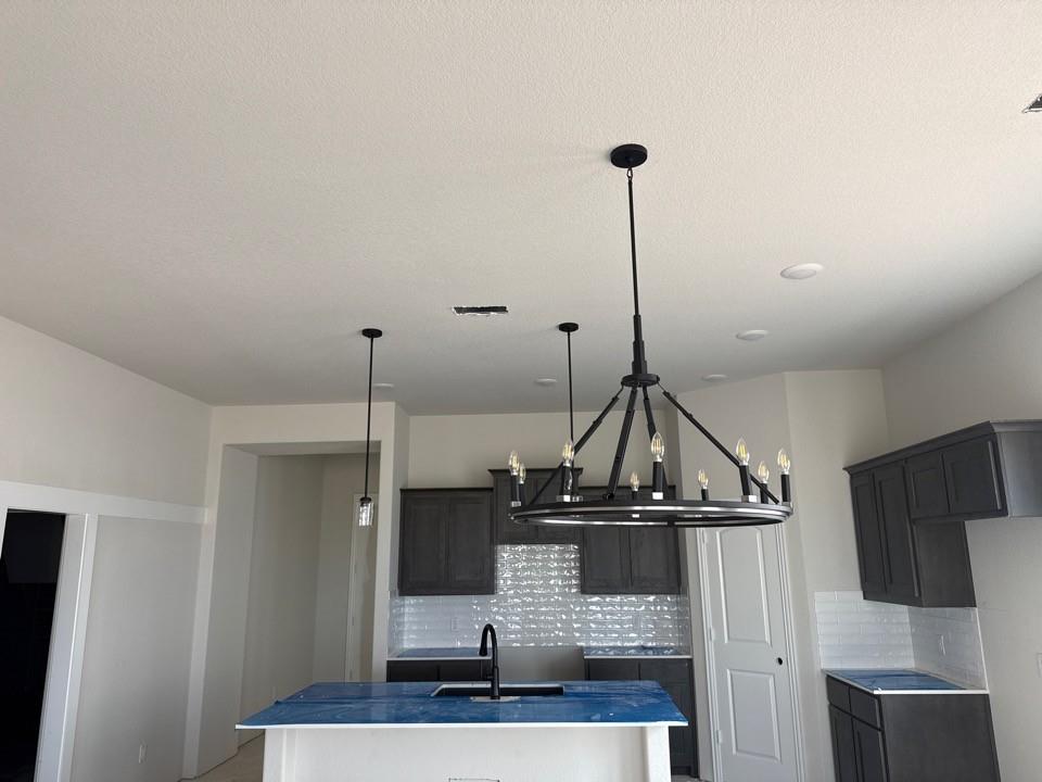 1213 Colca Drive Springtown, TX 76082 - Photo 3 of 8 Kitchen featuring a large circular chandelier, recessed lighting, dark cabinetry, white subway tile backsplash, and an island with a built-in sink and faucet
