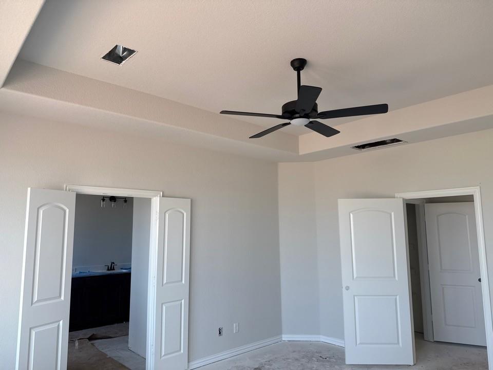 1213 Colca Drive Springtown, TX 76082 - Photo 5 of 8 Tray ceiling with a matte black ceiling fan, light gray wall paint, white two-panel interior doors, and white baseboards