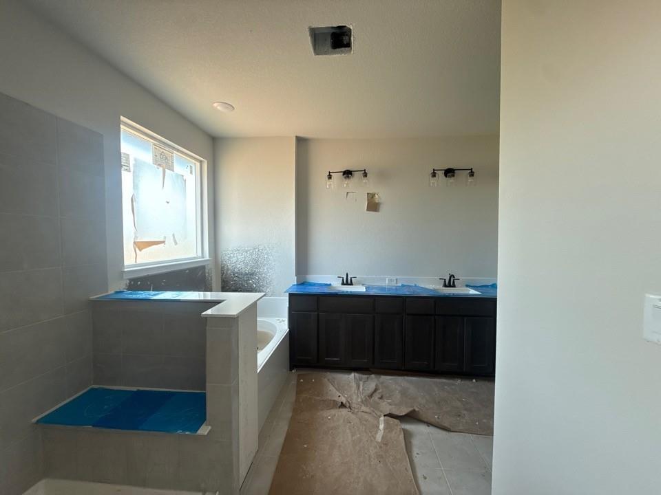1213 Colca Drive Springtown, TX 76082 - Photo 6 of 8 Bathroom featuring a built-in tub, separate shower enclosure with gray tile, and a double vanity with dark wood cabinetry and dual sinks
