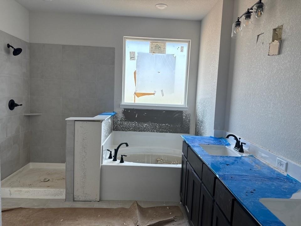 1213 Colca Drive Springtown, TX 76082 - Photo 7 of 8 Bathroom featuring a built-in tub, separate shower with gray tile surround, dark wood-finish vanity with dual sinks, and matte black fixtures