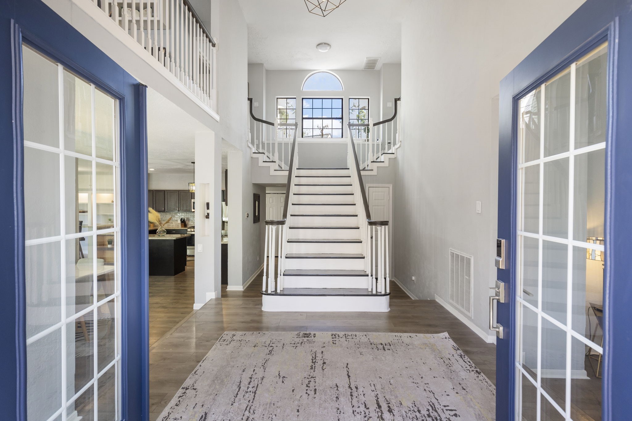 2110 Paso Rello Drive Houston, TX 77077 - Photo 4 of 41 This photo showcases a welcoming entryway with double doors leading to a spacious foyer. It features a grand staircase with elegant railings, high ceilings, and ample natural light from a large window above. The open layout provides a glimpse into a cozy living area and kitchen, highlighting beautiful wood flooring throughout.