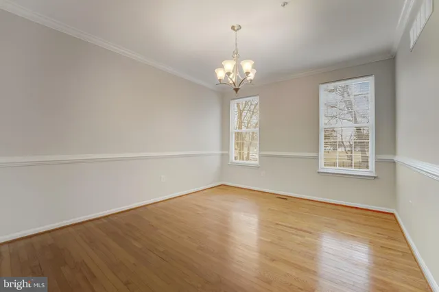 an empty room with wooden floor chandelier and windows