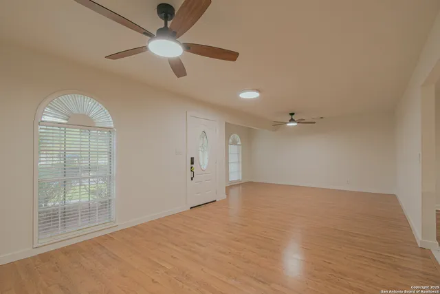 an empty room with wooden floor fan and windows