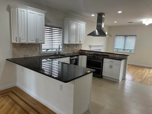a kitchen with granite countertop a stove a sink a refrigerator and white cabinets