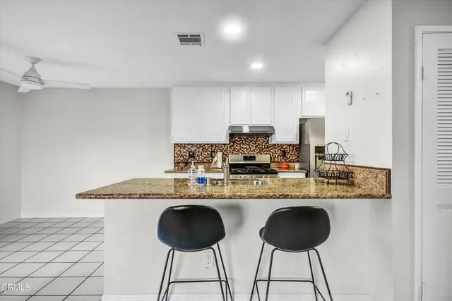 a kitchen with kitchen island granite countertop a counter space chairs cabinets and stainless steel appliances