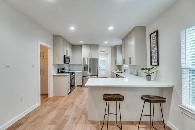 a large white kitchen with a refrigerator a stove a sink dishwasher and a dining table with wooden floor