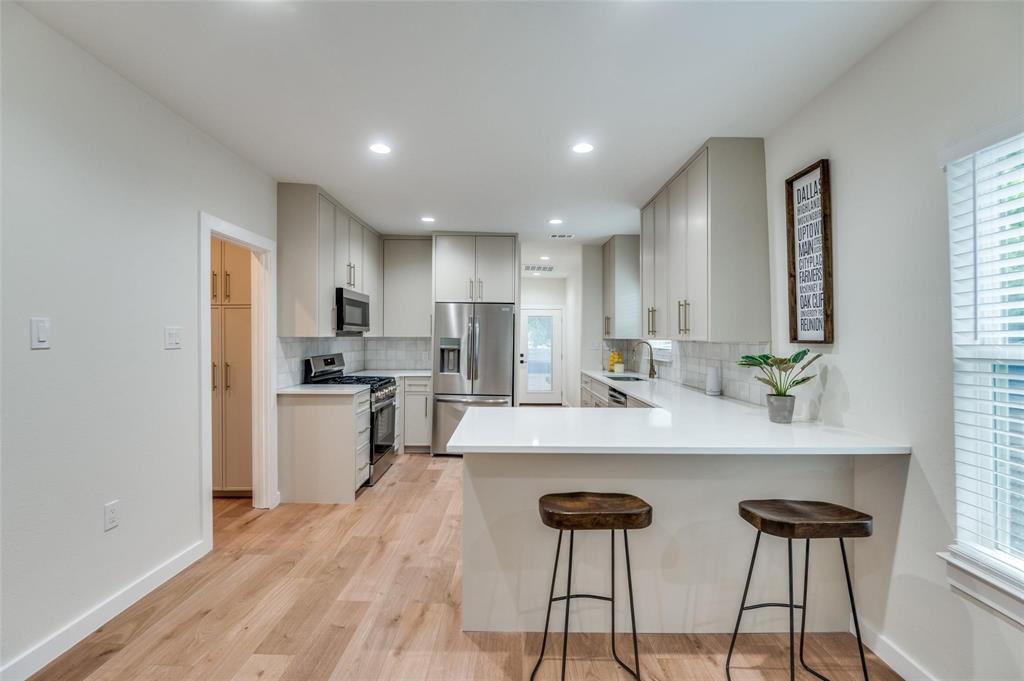 602 Brooks Avenue Dallas, TX 75208 - Photo 7 of 22 a large white kitchen with a refrigerator a stove a sink dishwasher and a dining table with wooden floor