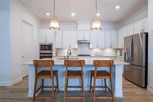 a kitchen with stainless steel appliances granite countertop a dining table chairs refrigerator and sink