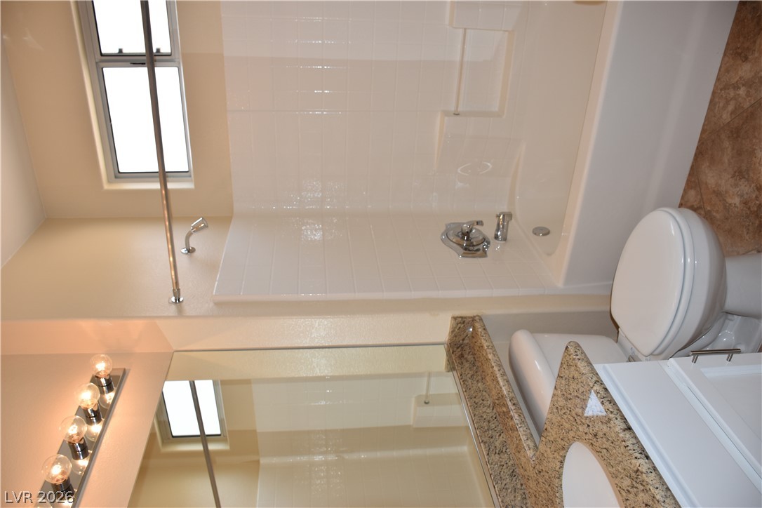 1680 Fieldbrook Street Henderson, NV 89052 - Photo 16 of 32 A classic bathtub and tiled shower alcove stand adjacent to a granite-topped vanity.