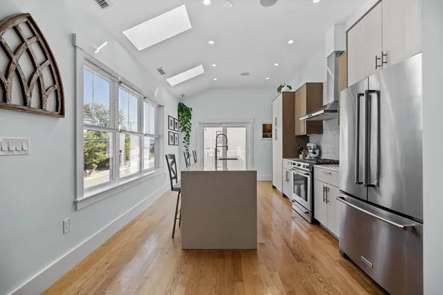 a living room with stainless steel appliances furniture wooden floor and a large window