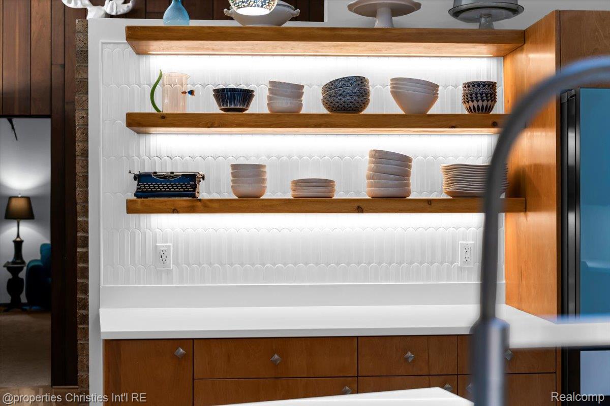 3939 Charing Cross Road Bloomfield Hills, MI 48304 - Photo 13 of 33 Kitchen featuring open wood shelving with integrated lighting, a unique white tile backsplash, light-toned countertops, and wood-finish cabinetry with decorative hardware