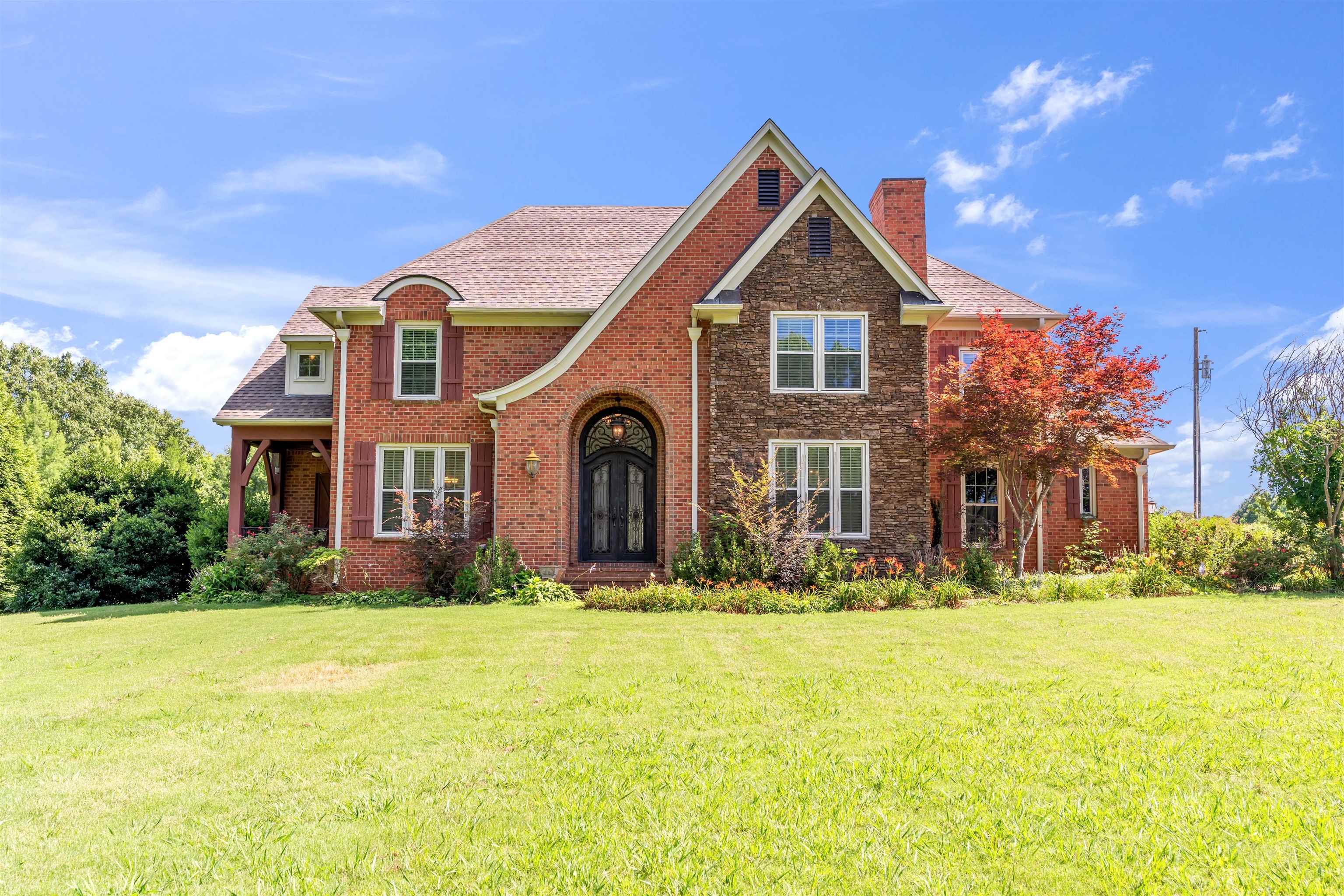 Brick and stone facade residence featuring a prominent arched entryway with double doors