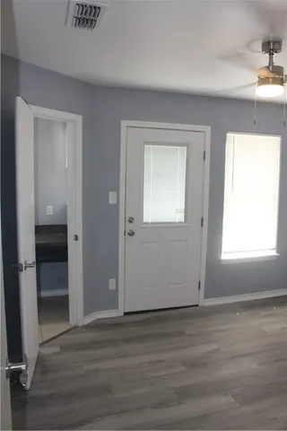 an empty room with wooden floor kitchen view and windows