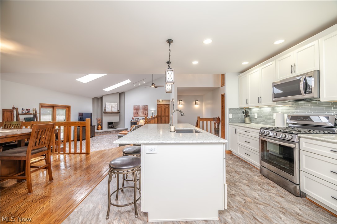 405 Airport Road Northwest Warren, OH 44481 - Photo 13 of 50 Kitchen featuring white cabinetry, stainless steel appliances, a light-toned countertop island with an undermount sink, and a glass tile backsplash