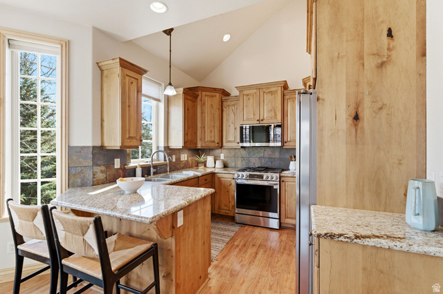 3026 Lower Saddleback Road Park City, UT 84098 - Photo 10 of 71 Kitchen featuring light stone counters, pendant lighting, appliances with stainless steel finishes, light wood-style flooring, and decorative backsplash