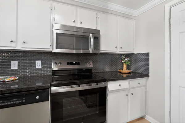 a kitchen with stainless steel appliances granite countertop white cabinets and a stove a window