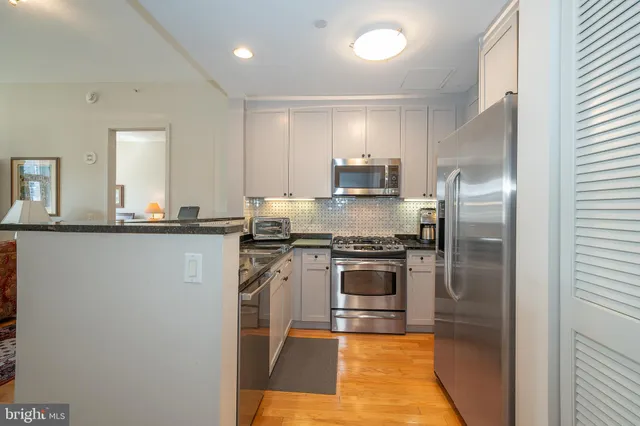 a kitchen with stainless steel appliances granite countertop a refrigerator a stove and a sink with wooden floor