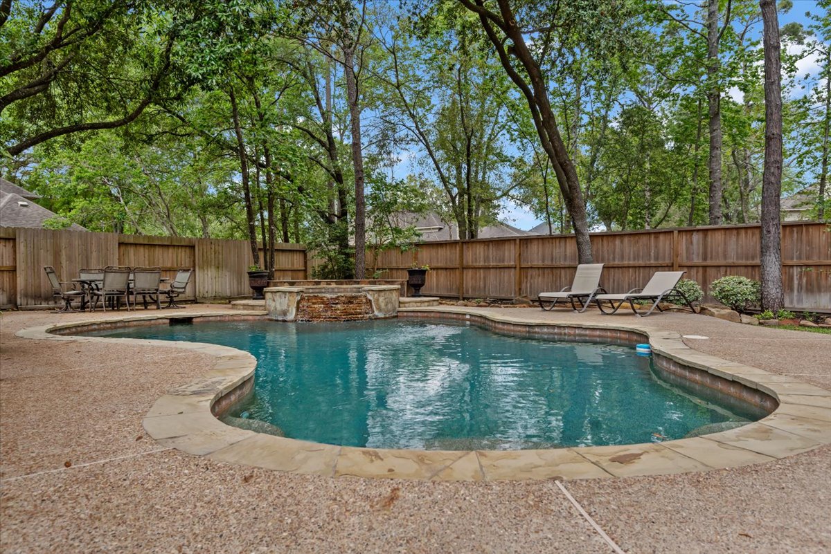15519 Stallion Point Circle Cypress, TX 77429 - Photo 36 of 37 The property features a private swimming pool with a stone waterfall, surrounded by a textured concrete deck and a wooden fence for privacy