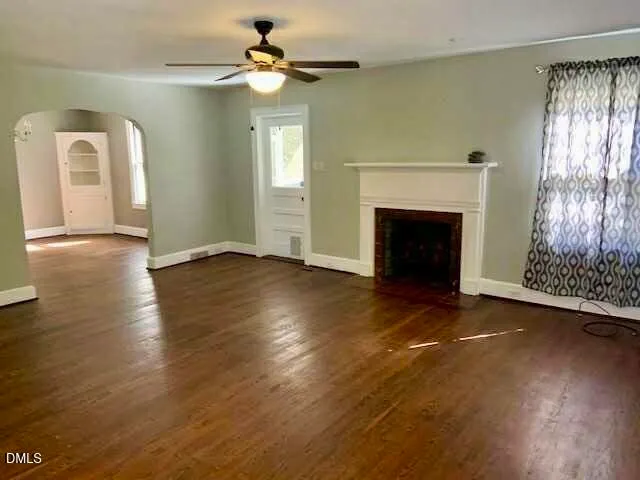 an empty room with wooden floor fireplace and windows