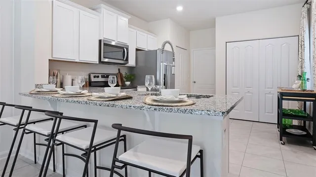 a kitchen with stainless steel appliances kitchen island granite countertop a table chairs in it and white cabinets