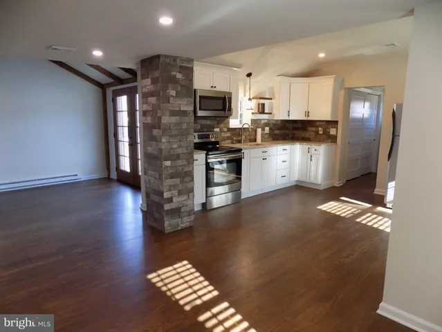 a view of kitchen with stainless steel appliances granite countertop a stove a sink a refrigerator white cabinets and wooden floor