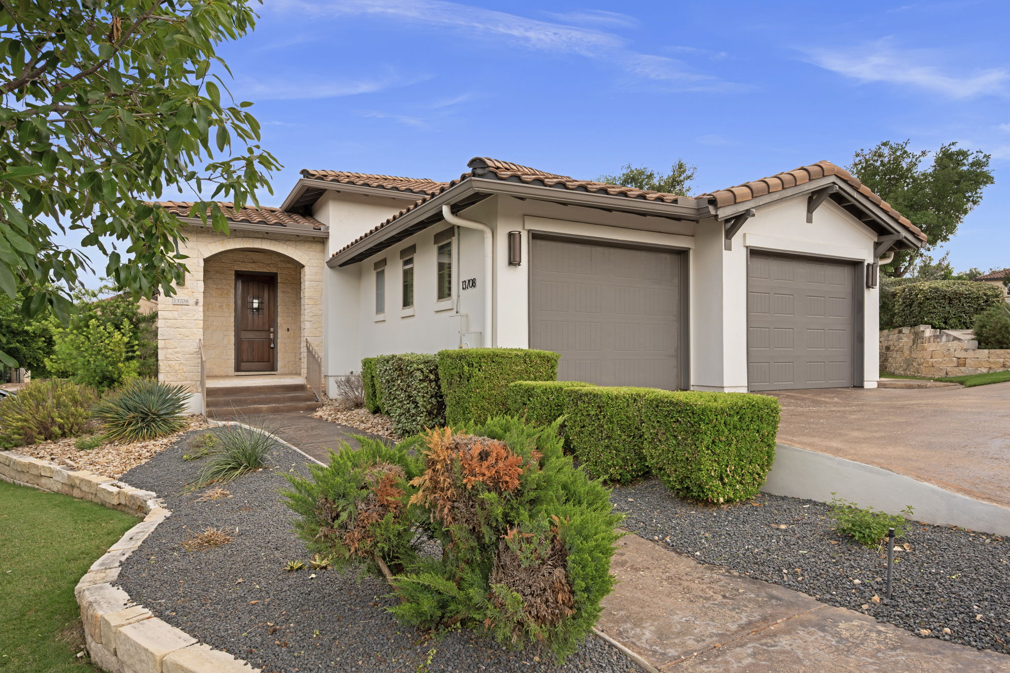 The property features a stucco exterior with a tiled roof, an arched entry with a wooden front door, and a driveway leading to two garage doors