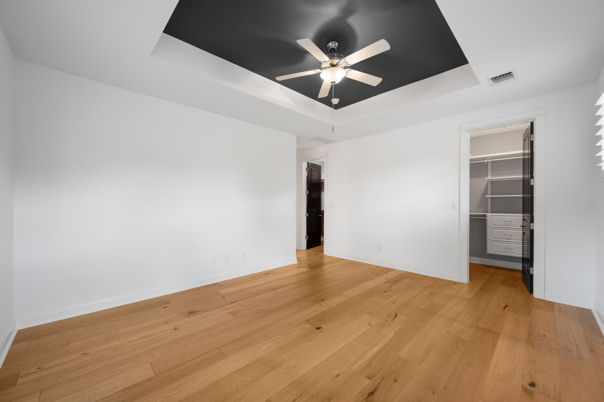 13708 Golden Wave Loop Austin, TX 78738 - Photo 18 of 34 This room features hardwood floors, a tray ceiling with a ceiling fan, and a walk-in closet with built-in shelving and drawers