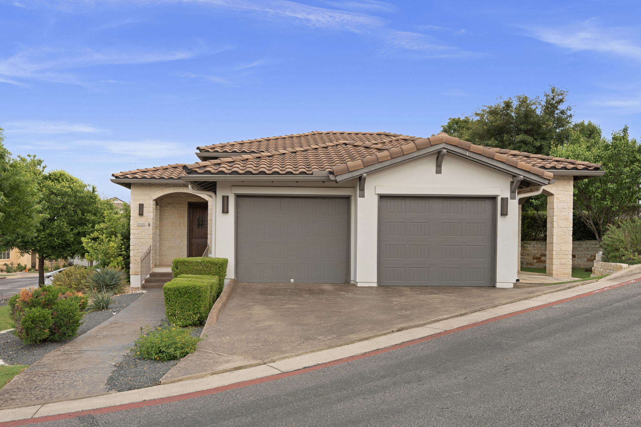 13708 Golden Wave Loop Austin, TX 78738 - Photo 2 of 34 The property features a two-car garage with grey doors, a paved driveway, and a tiled roof