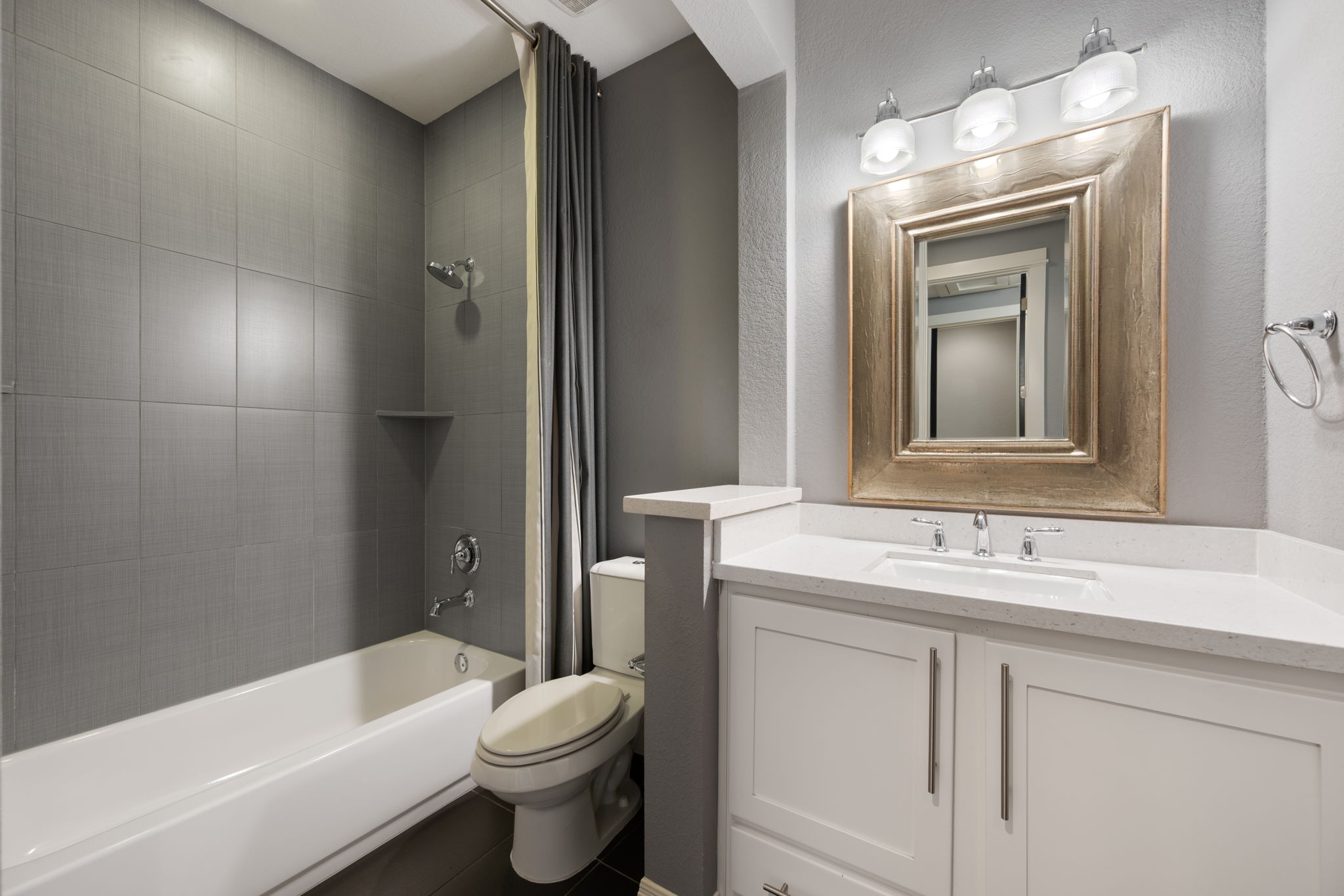 13708 Golden Wave Loop Austin, TX 78738 - Photo 27 of 34 The bathroom features a white vanity with a white countertop and a framed mirror, alongside a bathtub and shower area with gray tiled walls