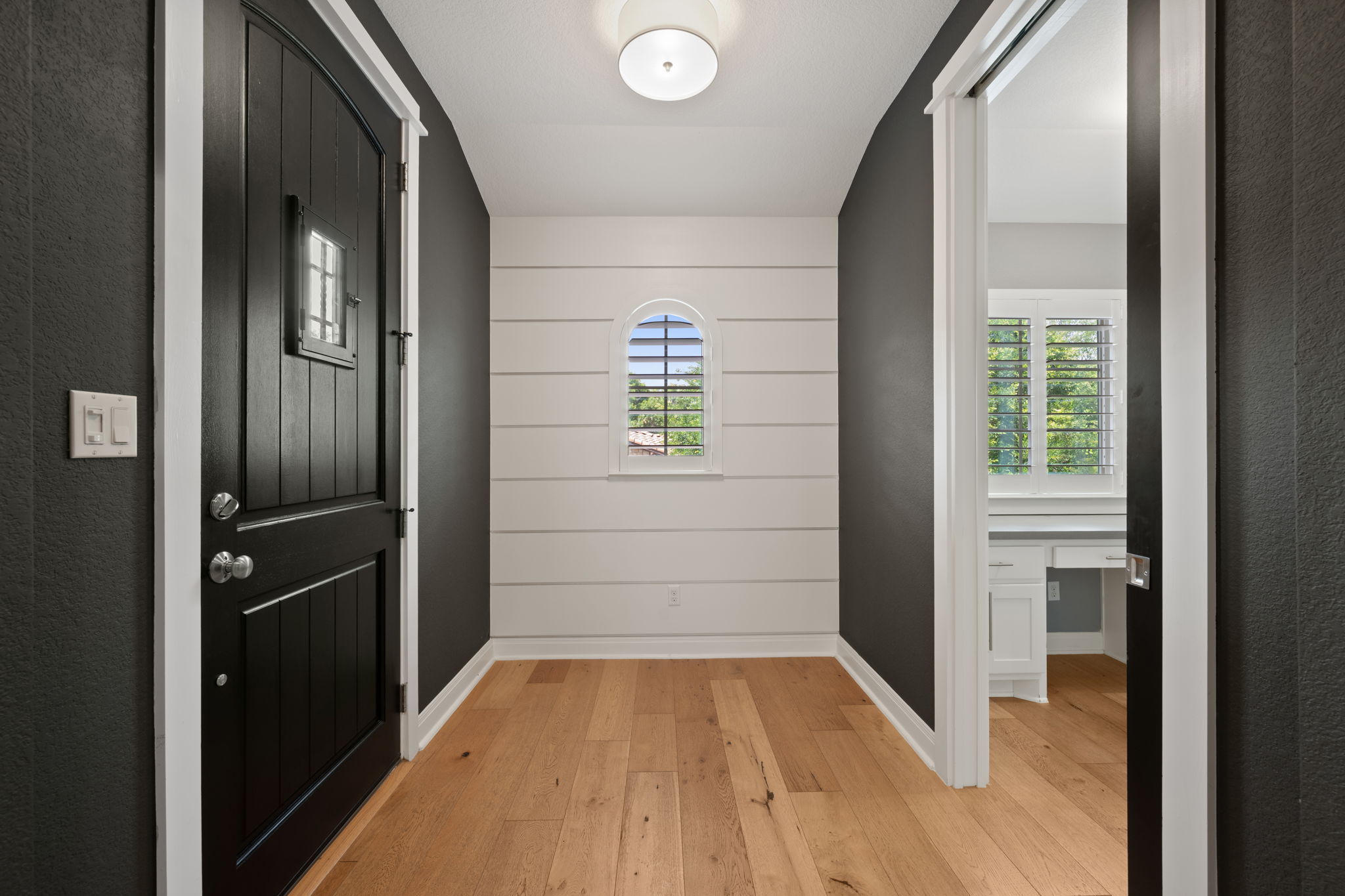 13708 Golden Wave Loop Austin, TX 78738 - Photo 28 of 34 The entry features a dark panel door with a small window, light wood flooring, and a white shiplap accent wall with an arched window