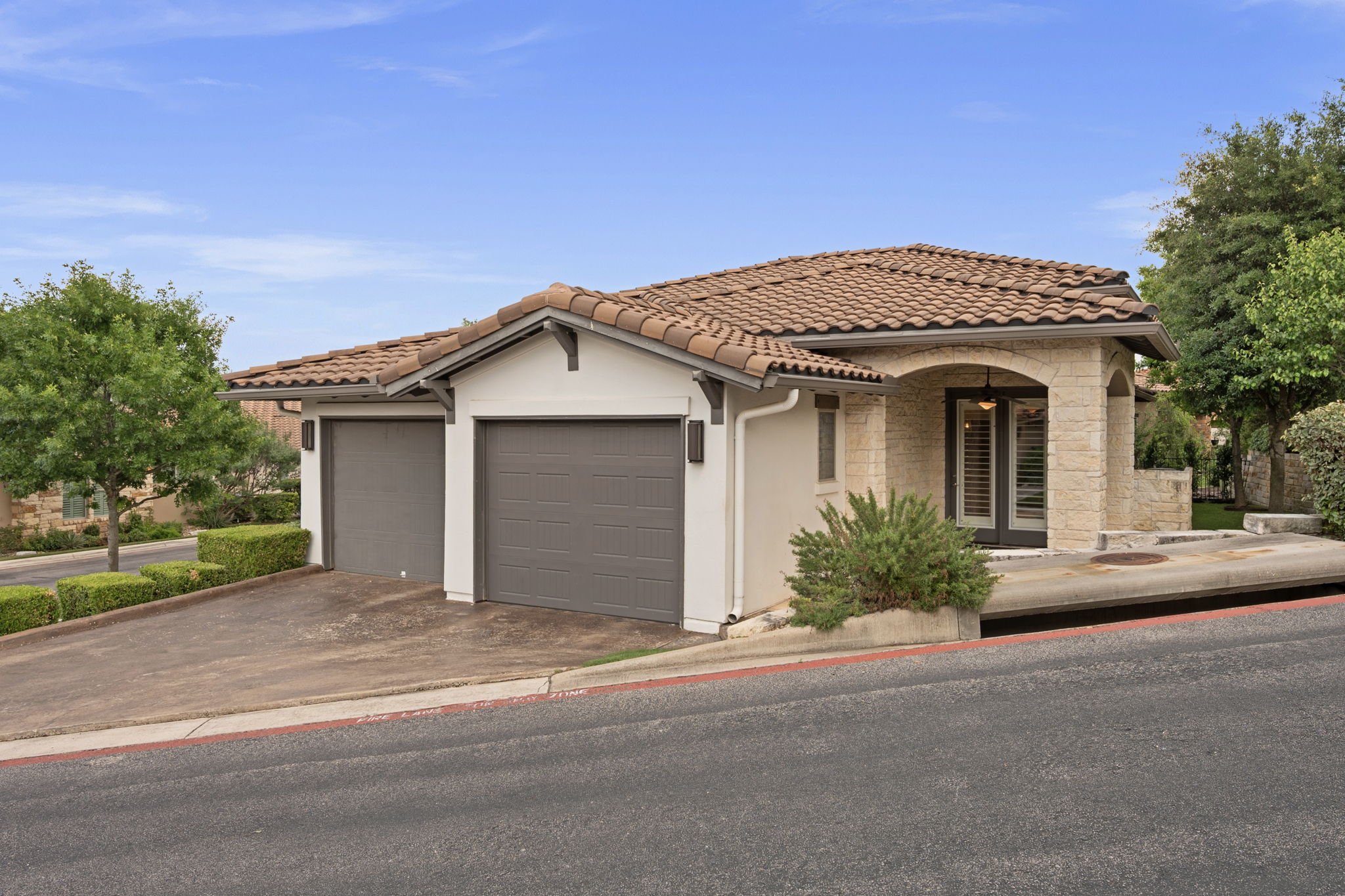 13708 Golden Wave Loop Austin, TX 78738 - Photo 3 of 34 The property features a tile roof, an arched entry with a glass door and shutters, and an attached garage with two garage doors