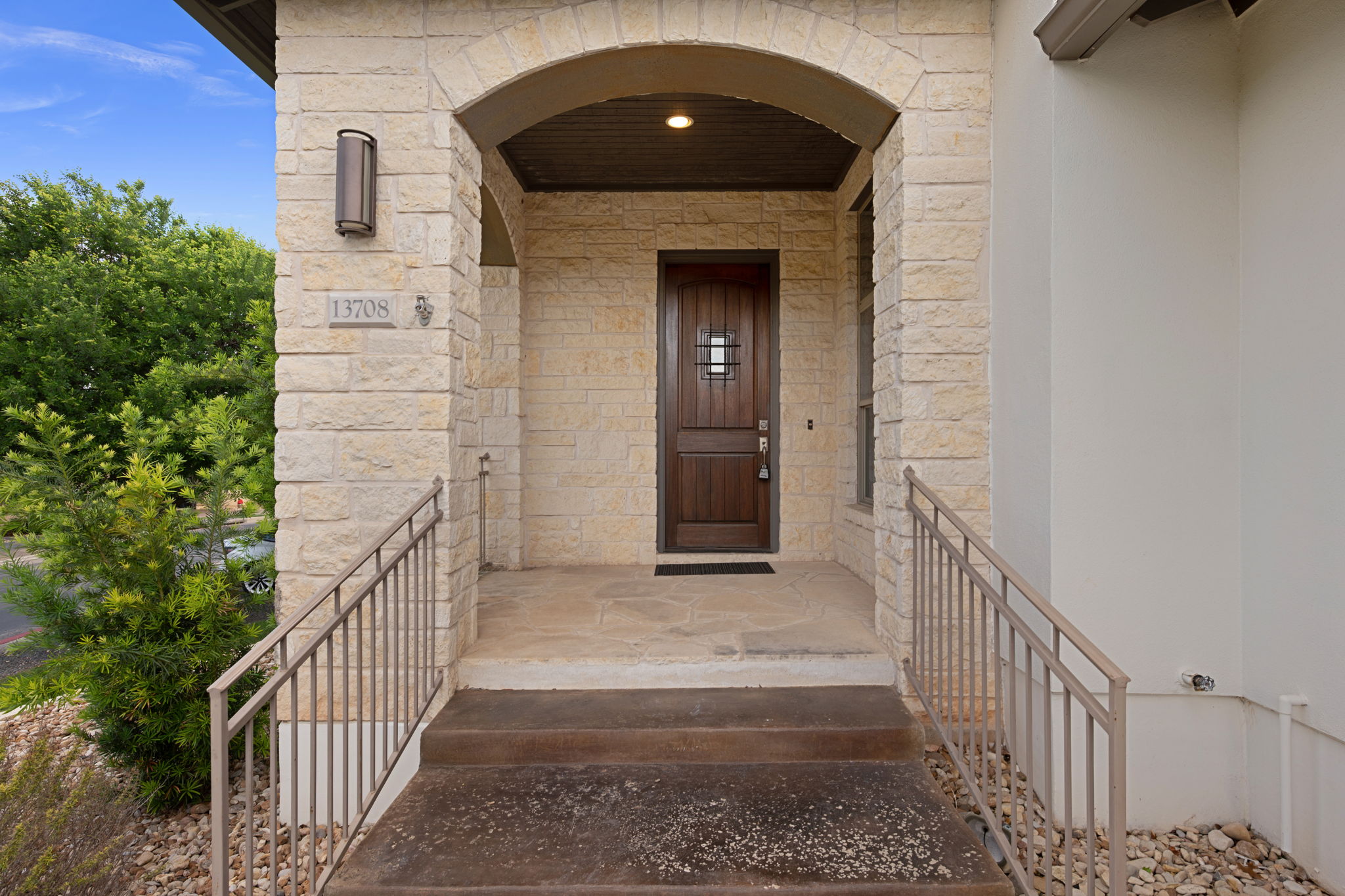 13708 Golden Wave Loop Austin, TX 78738 - Photo 4 of 34 The property features a stone facade, an arched entry, a dark wood front door with a small window, and metal handrails leading to the entrance