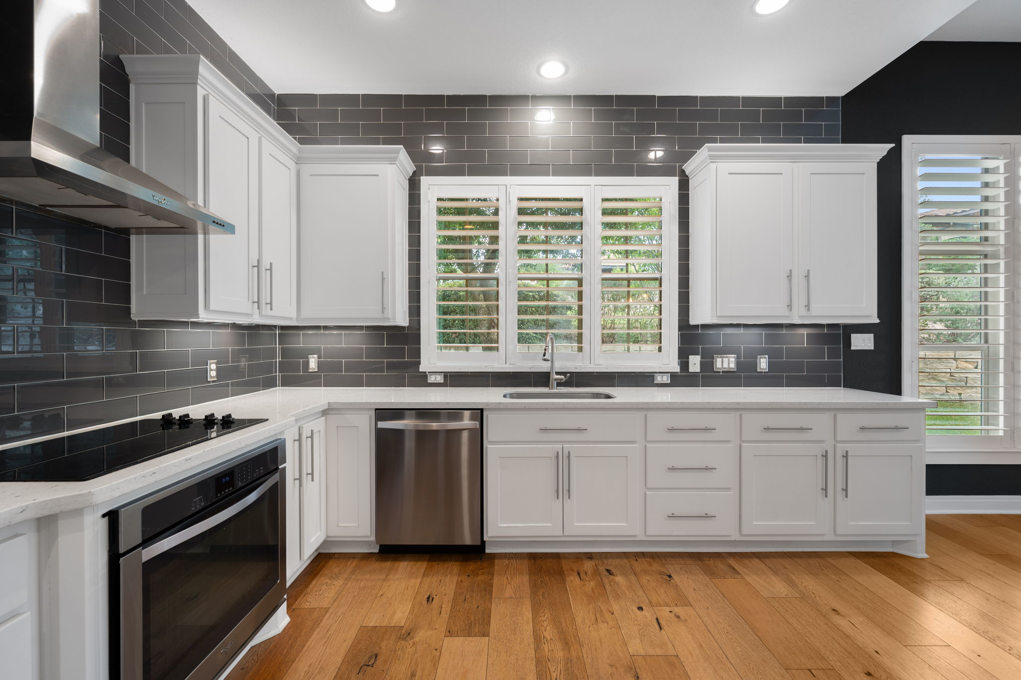 13708 Golden Wave Loop Austin, TX 78738 - Photo 8 of 34 The kitchen features white cabinetry, a dark subway tile backsplash, light-colored countertops, and stainless steel appliances, complemented by hardwood flooring